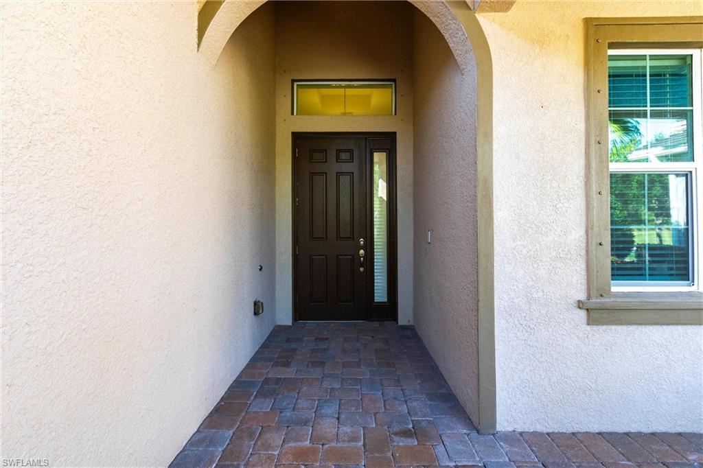 Covered entry featuring a dark paneled door with a sidelight, a transom window, and a brick paver pathway