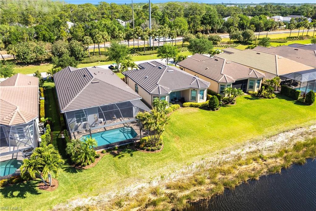 Residential property featuring a screened-in swimming pool, a private screened lanai, a tile roof, a lush green lawn, and a water feature bordering the property