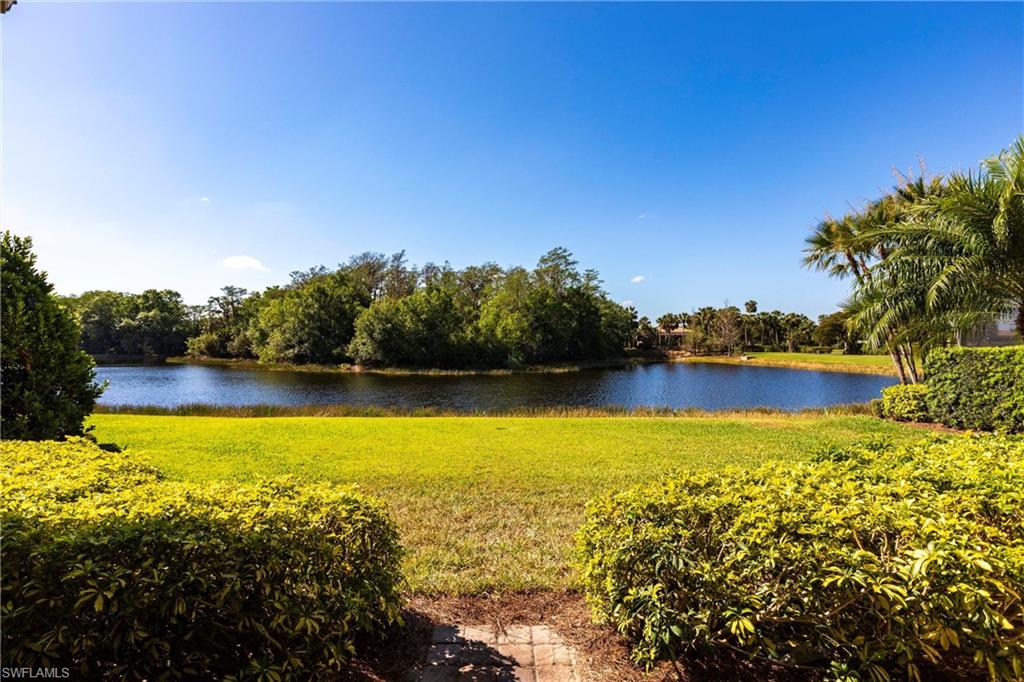 Lakefront property featuring expansive green lawn, mature landscaping, and a clear blue sky