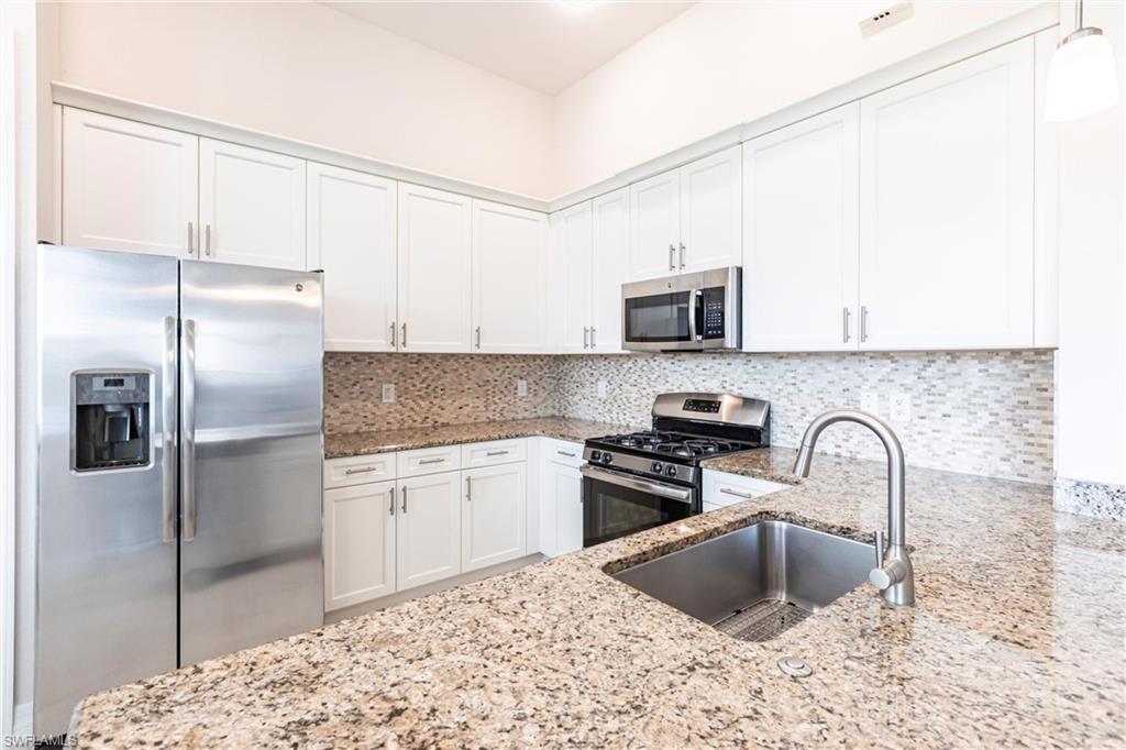 Bright kitchen featuring white shaker cabinetry, stainless steel appliances, speckled stone countertops, and a mosaic tile backsplash