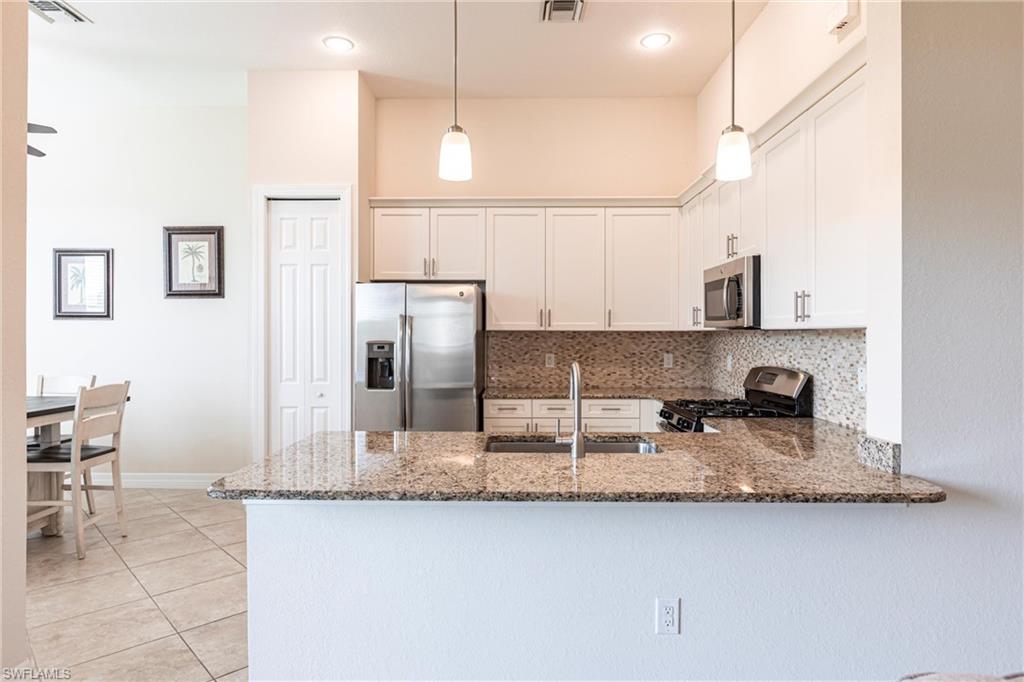Kitchen featuring a peninsula with a stone countertop and undermount sink, stainless steel appliances, white cabinetry, and a mosaic tile backsplash