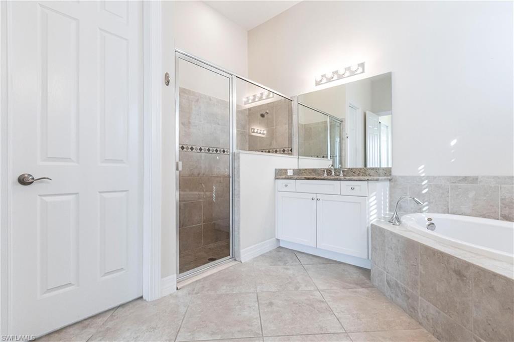 Spacious bathroom featuring a glass-enclosed shower, a separate soaking tub, and a vanity with a stone countertop