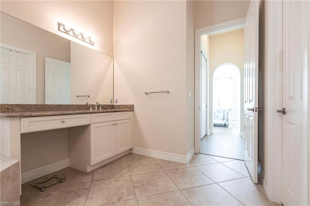 Dual vanity with a stone countertop, integrated sinks, custom cabinetry, and a full-width mirror