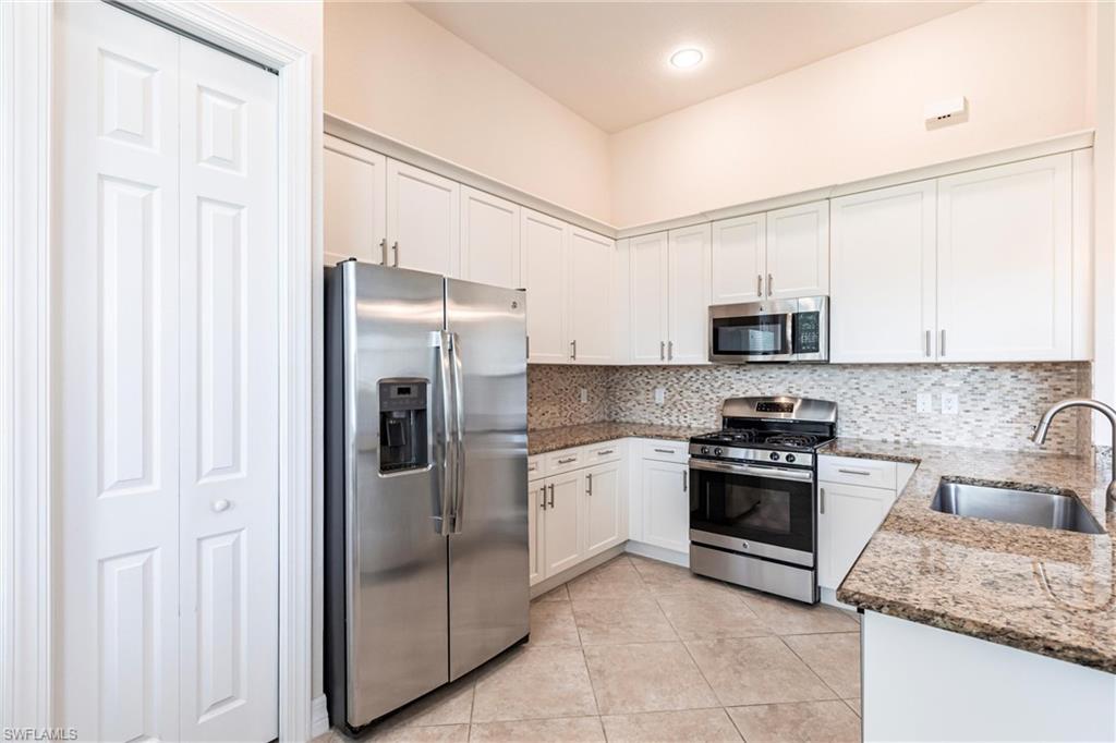 Kitchen featuring white cabinetry, stainless steel appliances, speckled stone countertops, a mosaic tile backsplash, and tile flooring