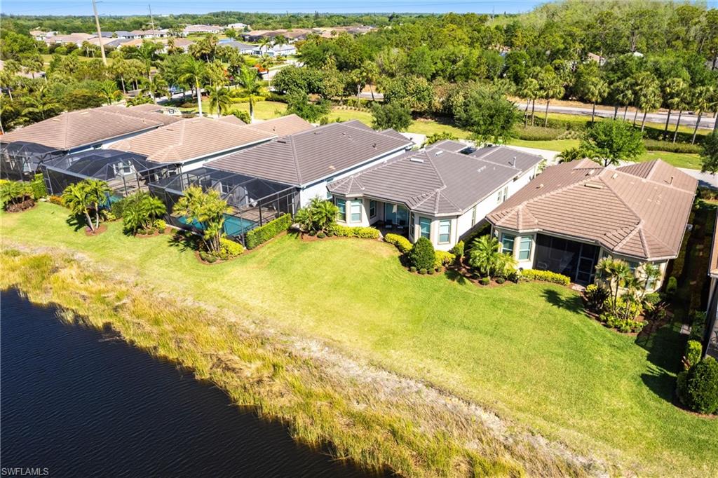 Waterfront property featuring a screened-in lanai with a private pool, lush green lawn, mature landscaping, and a tile roof