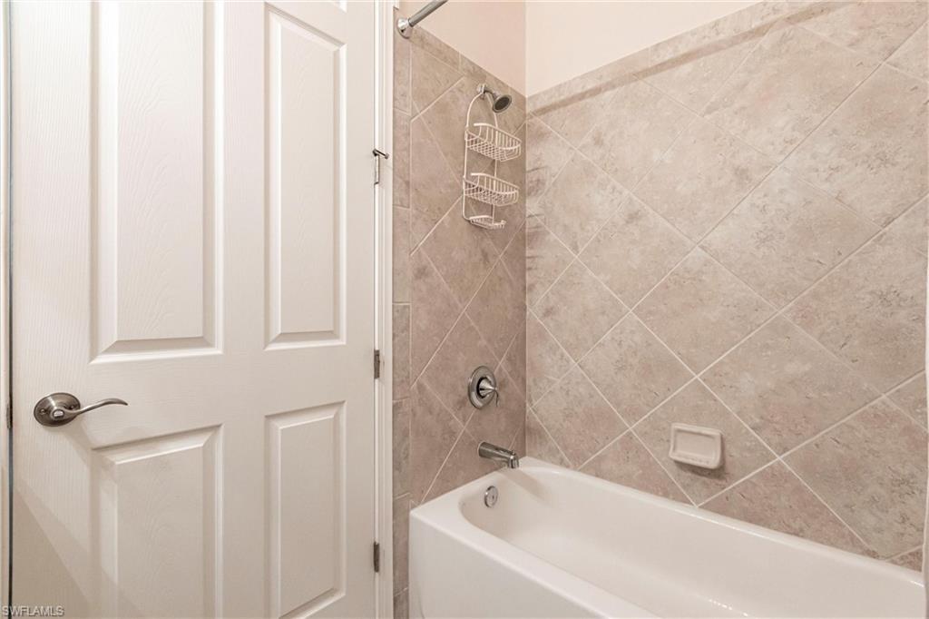 White bathtub featuring a shower with diagonal tile surround and brushed nickel fixtures