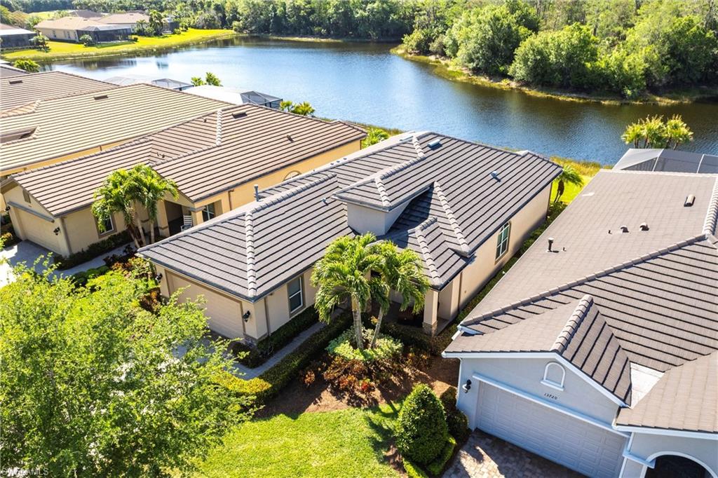 Lakeside property featuring a tiled roof, attached garage, manicured landscaping, and mature palm trees