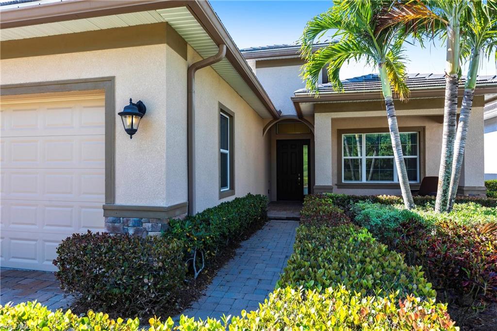 Stucco exterior with stone accenting, a paver walkway, and a landscaped entry