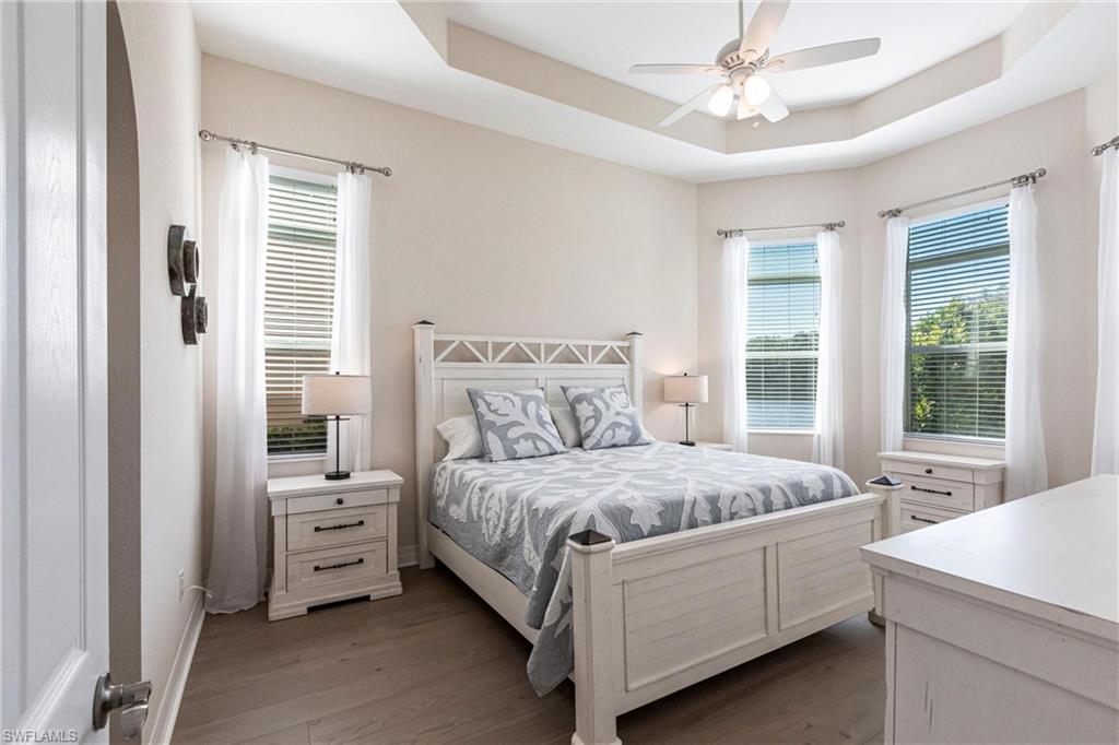 Recessed tray ceiling with ceiling fan, multiple windows with blinds and sheer curtains, wood-finish flooring, and arched doorway