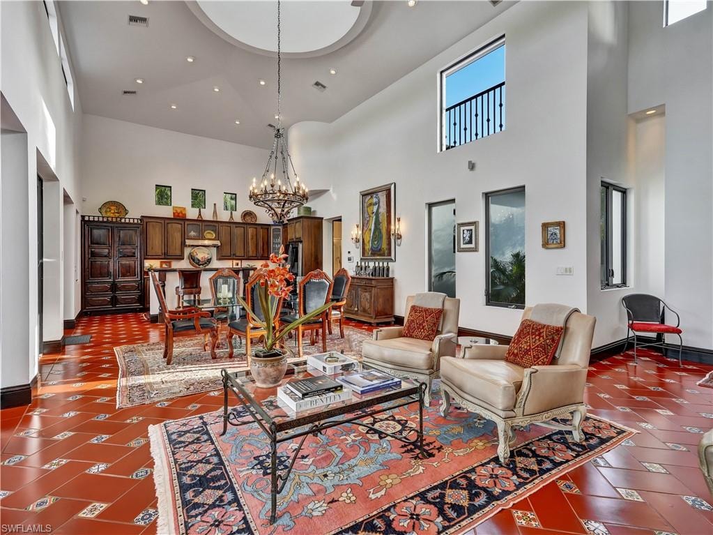 Spacious living area featuring terra cotta tile flooring with decorative inserts, a grand chandelier, and a recessed ceiling dome