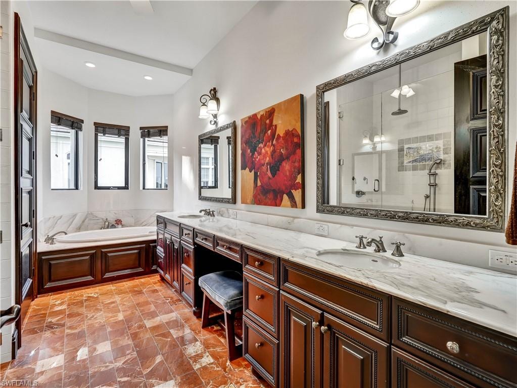 Dual vanity with undermount sinks and marble countertops, rich wood cabinetry, a built-in garden tub, and decorative floor tiling