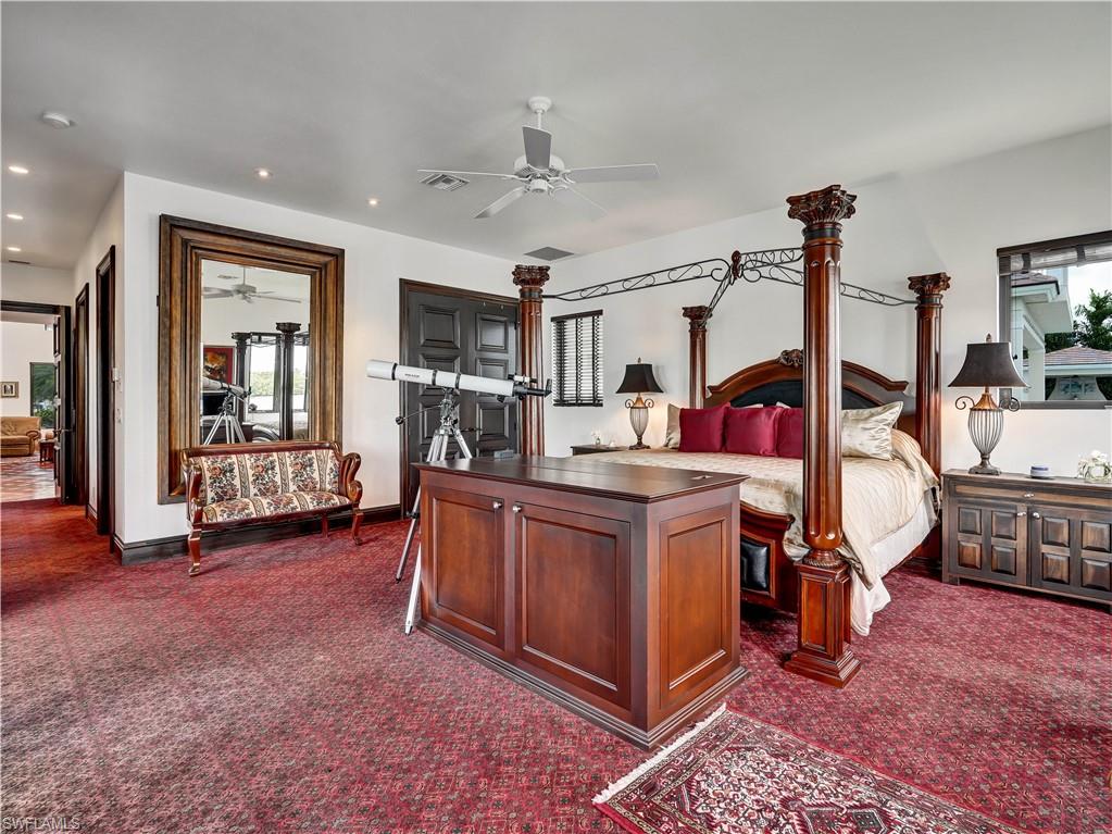 Spacious room featuring red patterned carpeting, a ceiling fan, recessed lighting, a large wall mirror with a carved wood frame, and a dark wood four-poster bed