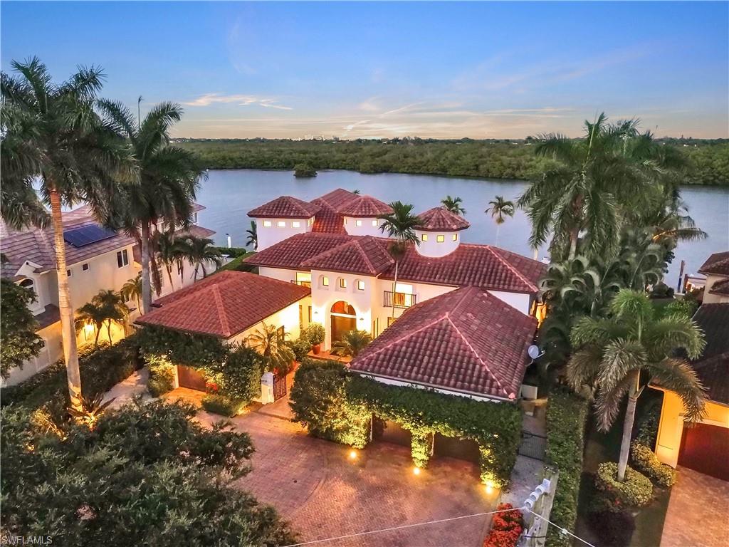 Waterfront property featuring a Mediterranean-inspired exterior with multiple red tile roofs, a circular turret, arched entryways, and a paver driveway