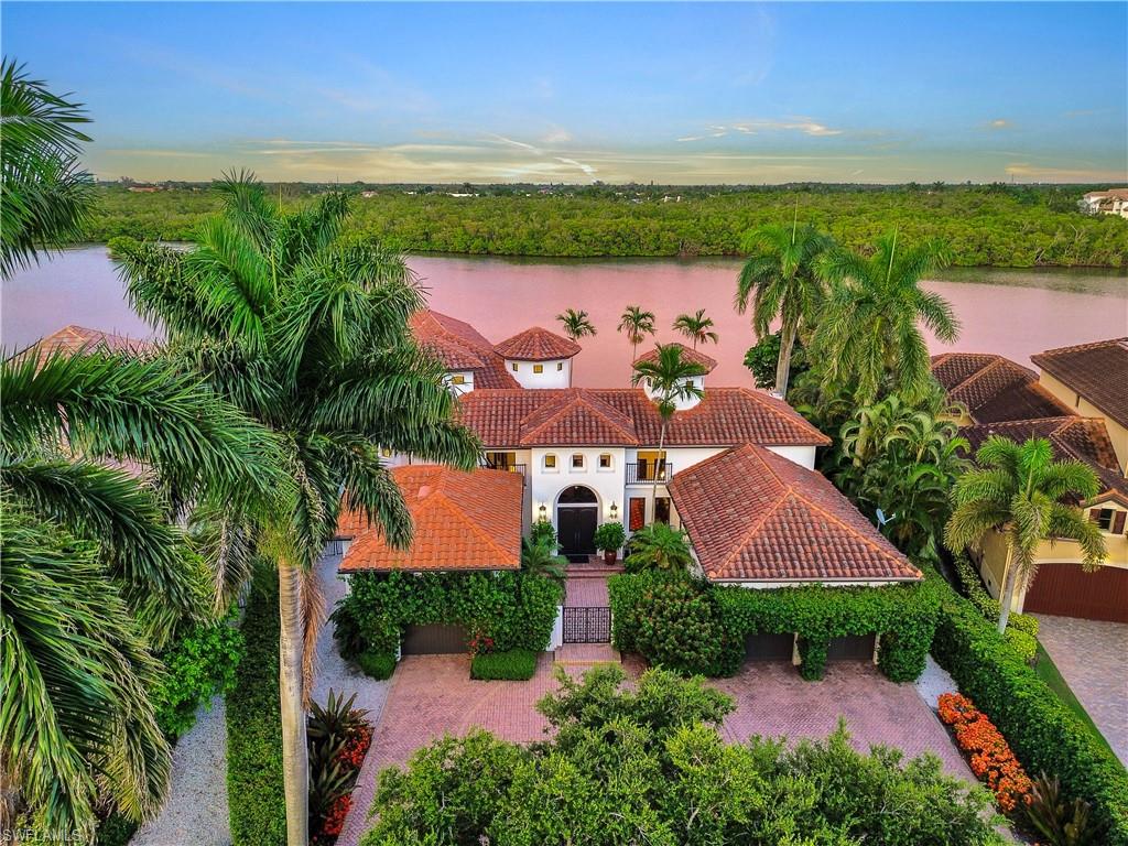 Mediterranean-style residence featuring a terracotta tile roof, white stucco exterior, and lush tropical landscaping