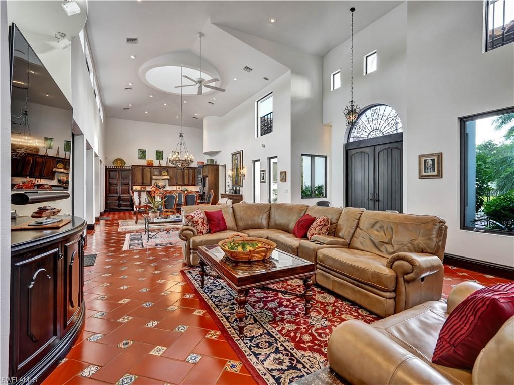 Spacious great room featuring high vaulted ceilings, terracotta-style flooring with decorative inlays, a prominent double-door entry with an arched transom, and recessed lighting throughout