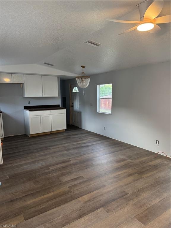 Open-concept living area featuring wood-finish flooring, white cabinetry with dark countertops, a decorative chandelier, and a ceiling fan with integrated lighting