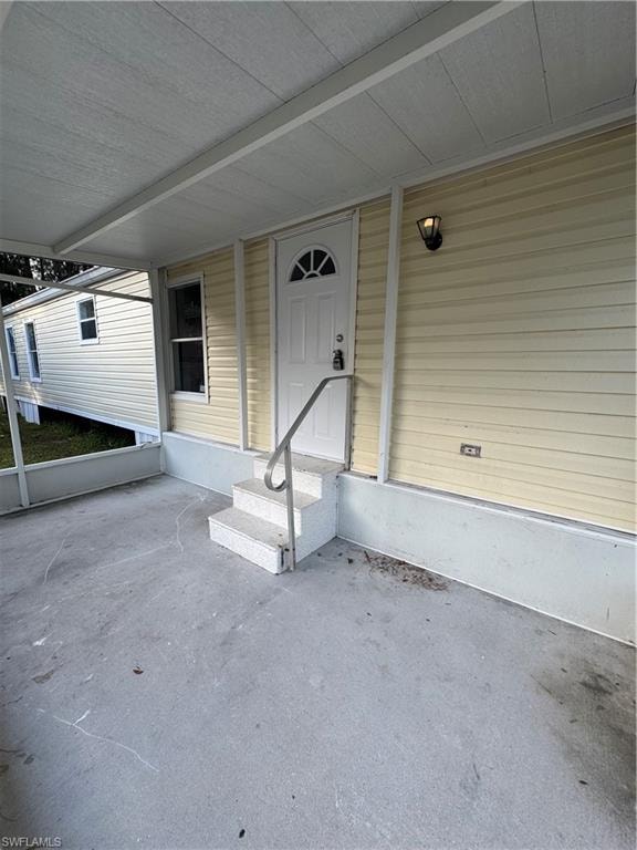 Covered porch entry featuring a decorative paneled door with an arched window insert, exterior wall light fixture, and a three-step entry with a metal handrail