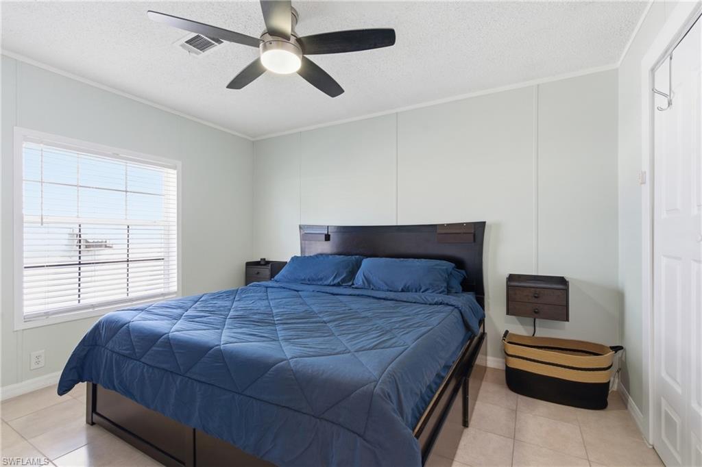 Bedroom featuring a large window with horizontal blinds, a ceiling fan with integrated lighting, wood-finish flooring, paneled walls, and a white interior door