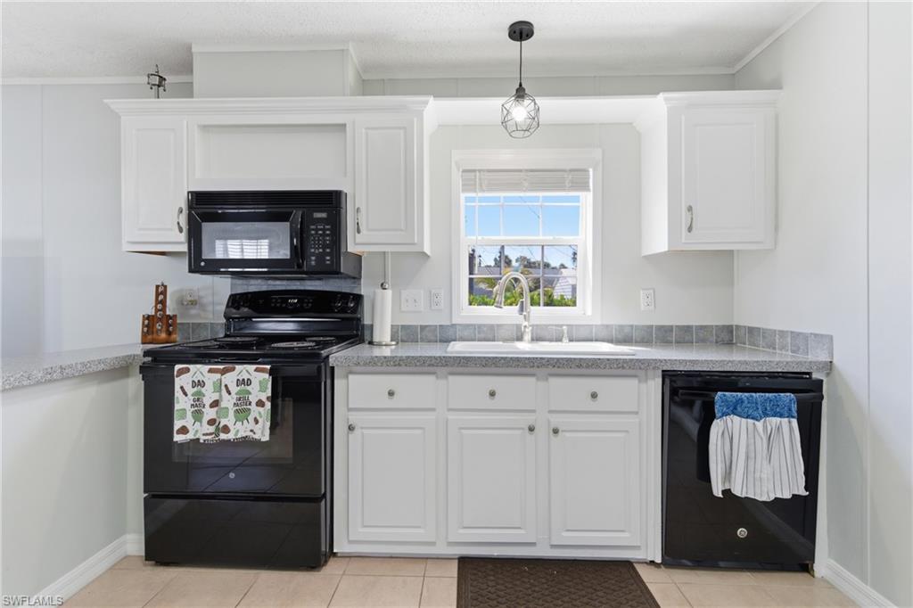 Kitchen featuring white cabinetry, black appliances including a built-in microwave and dishwasher, a stainless steel sink, and gray countertops with a tiled backsplash