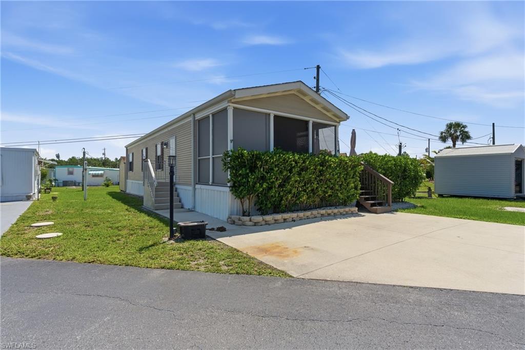 Exterior featuring a screened porch, mature privacy landscaping, concrete driveway, and a detached storage shed