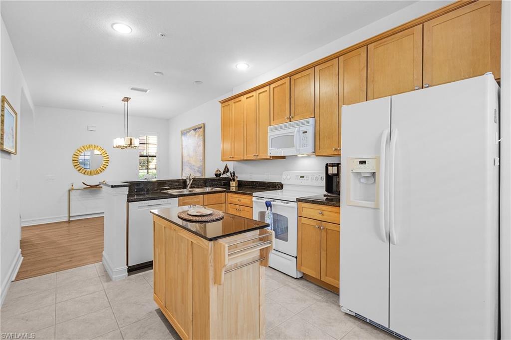 Kitchen with white appliances, a sink, a peninsula, dark countertops, and light tile patterned floors