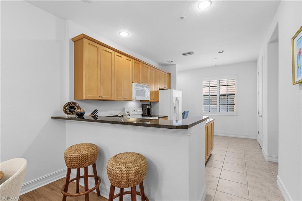 Kitchen featuring white appliances, dark countertops, a peninsula, baseboards, and a kitchen breakfast bar