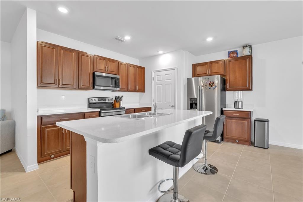 Kitchen with a kitchen bar, brown cabinetry, appliances with stainless steel finishes, light countertops, and light tile patterned floors