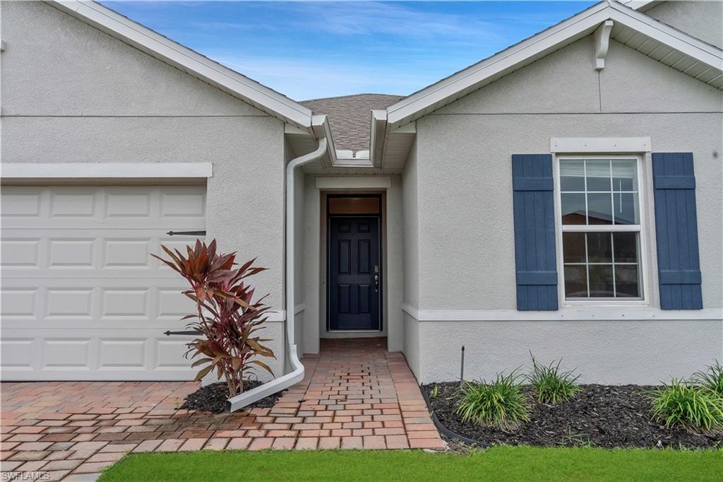 View of front of home with stucco siding, a garage, and roof with shingles