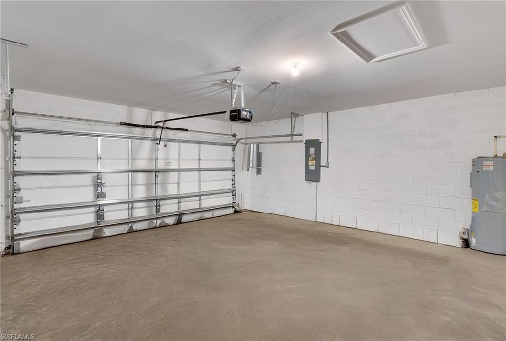 Garage with concrete block wall, electric water heater, electric panel, and a garage door opener