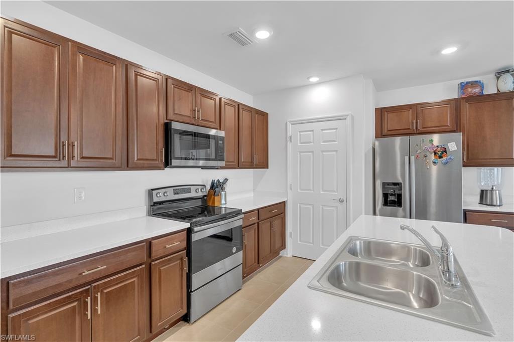 Kitchen featuring appliances with stainless steel finishes, brown cabinets, light tile patterned flooring, recessed lighting, and light stone countertops