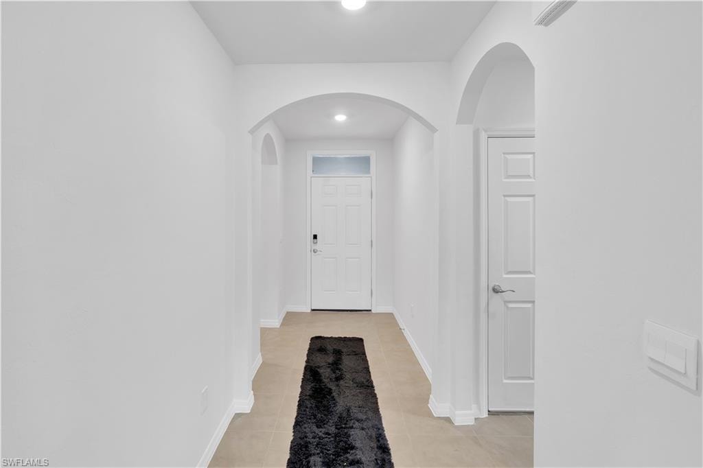 Corridor featuring arched walkways, light tile patterned flooring, and recessed lighting