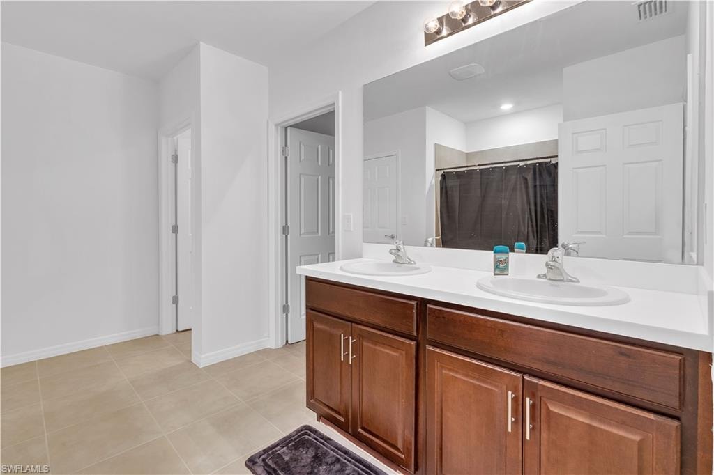 Full bath featuring double vanity, light tile patterned floors, and a shower with curtain