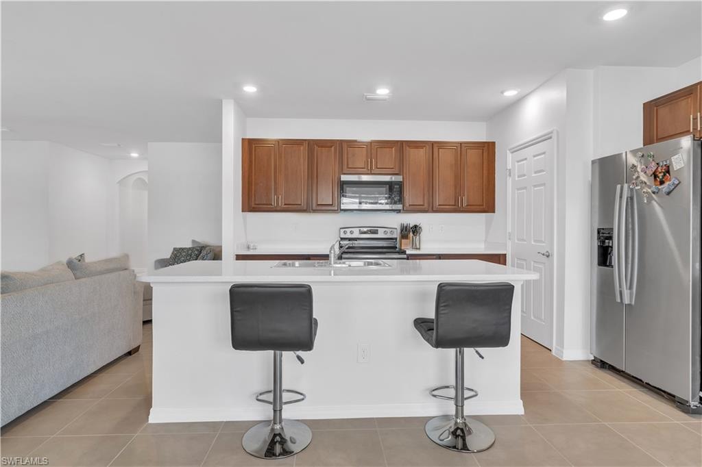 Kitchen with appliances with stainless steel finishes, light tile patterned floors, a kitchen breakfast bar, arched walkways, and recessed lighting