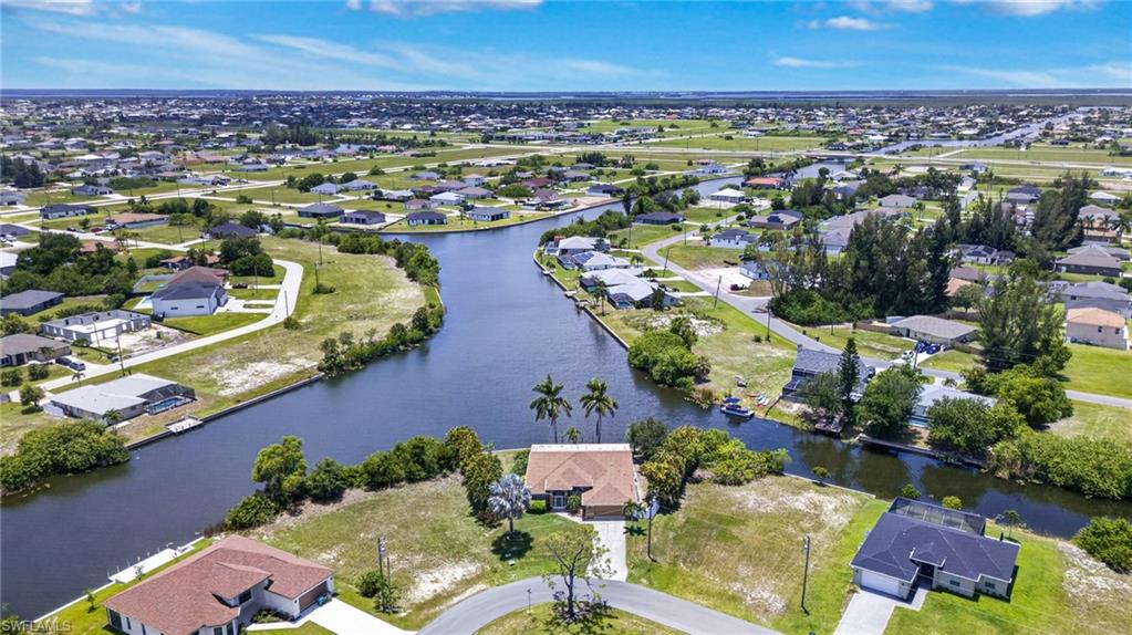 Aerial perspective showcasing a residential area featuring multiple canals, single-story homes with various rooflines, mature trees, and undeveloped lots