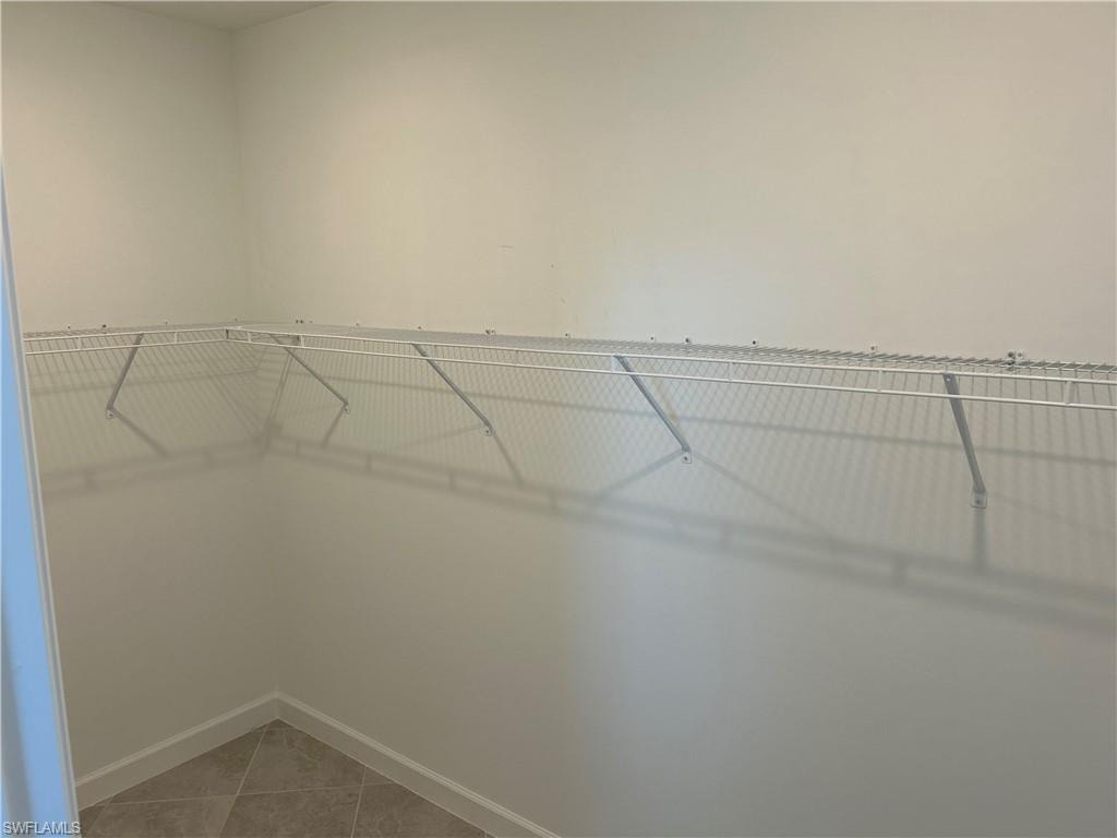 Corner closet featuring white wire shelving, light neutral wall paint, and tiled flooring with coordinating baseboards