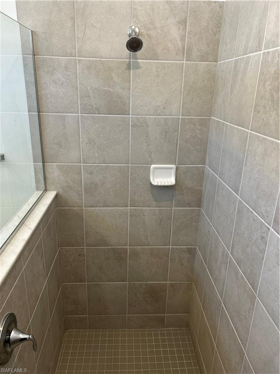Tiled shower enclosure featuring a glass panel, chrome showerhead, and coordinating floor tiles