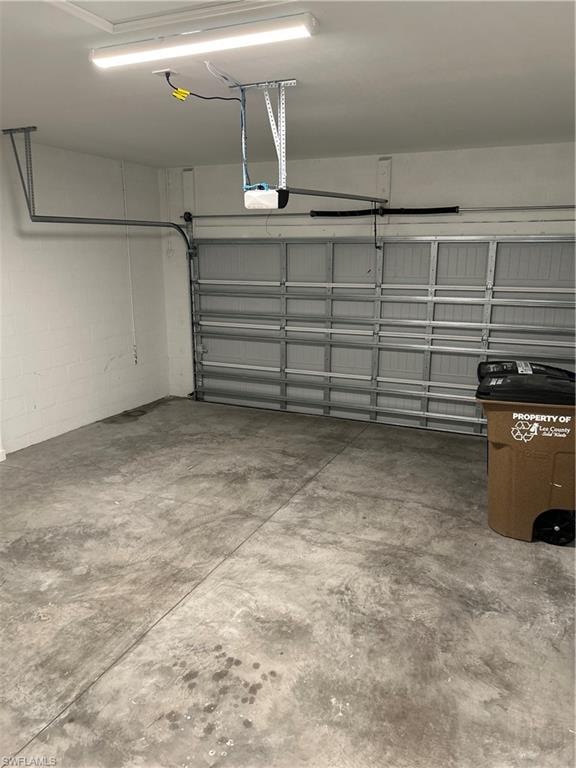 Garage space featuring a roll-up door, exposed ceiling-mounted garage door opener, concrete flooring, and ceiling-mounted strip lighting
