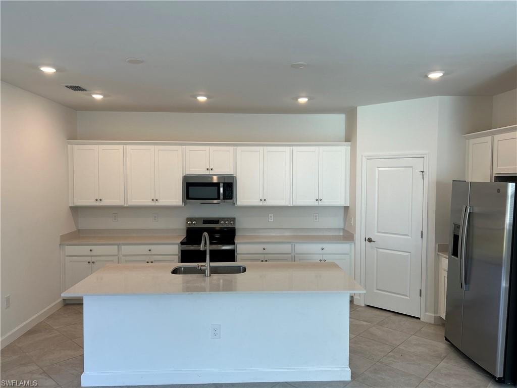 Modern kitchen featuring a central island with an undermount sink, white shaker-style cabinetry, stainless steel appliances, recessed lighting, and tile flooring
