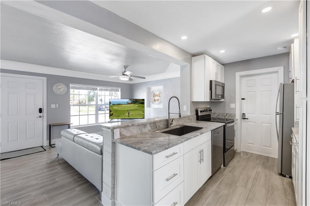 Modern kitchen featuring white cabinetry, stone countertops, stainless steel appliances, and a built-in sink with a gooseneck faucet