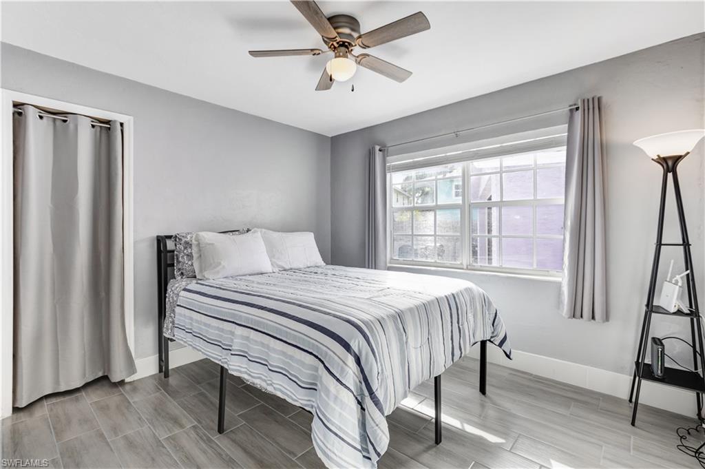 Room featuring wood-finish tile flooring, a multi-pane window with privacy blinds and drapes, a ceiling fan with integrated lighting, and a closet with a curtain closure