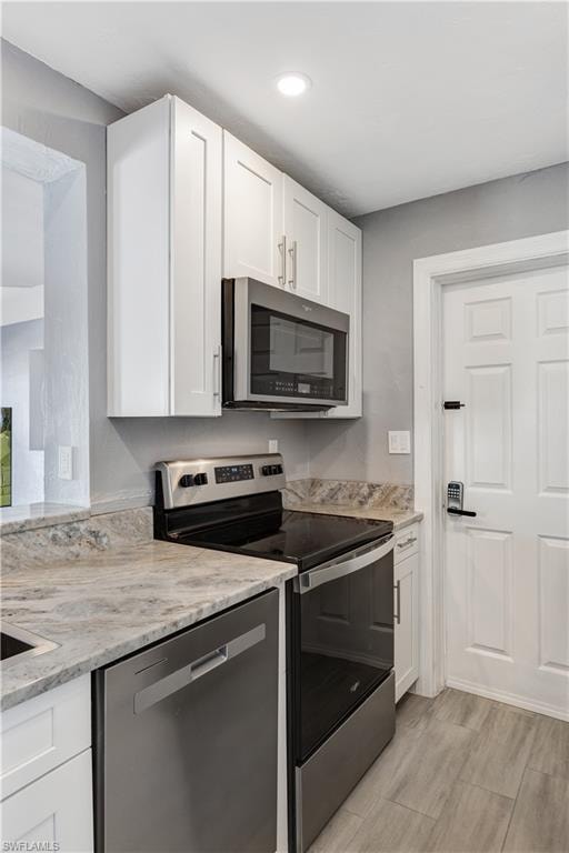 Kitchen featuring white shaker cabinetry, stainless steel appliances, patterned stone countertops, and wood-finish flooring