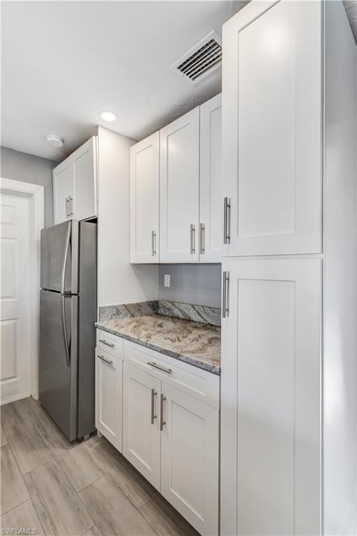 Kitchen featuring shaker-style white cabinetry with brushed nickel hardware, light-toned stone countertops, a full-height backsplash, and wood-finish flooring