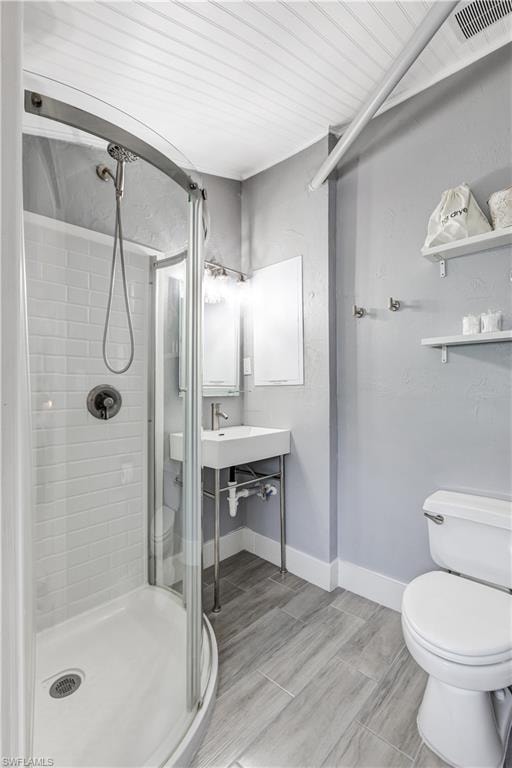 Contemporary bathroom featuring a curved glass shower enclosure with subway tile surround, a modern pedestal sink, and plank-style tile flooring