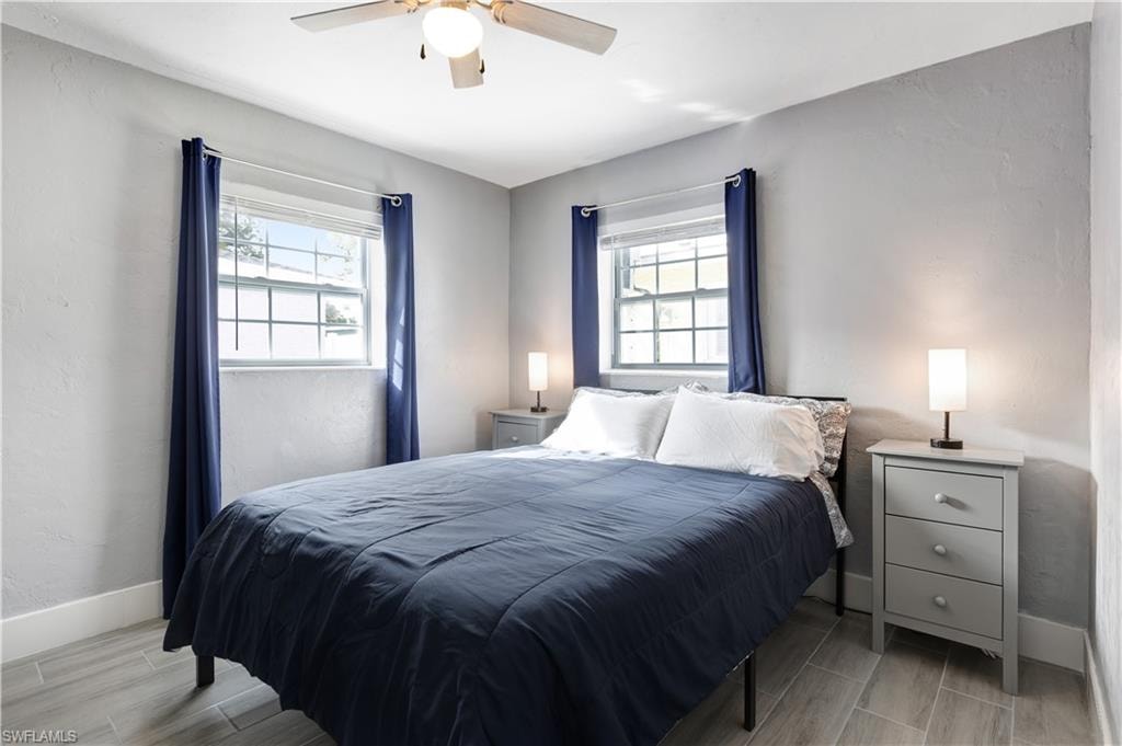 Light-filled bedroom featuring two large windows with mullions, wood-finish flooring, a ceiling fan with integrated lighting, and neutral wall finishes