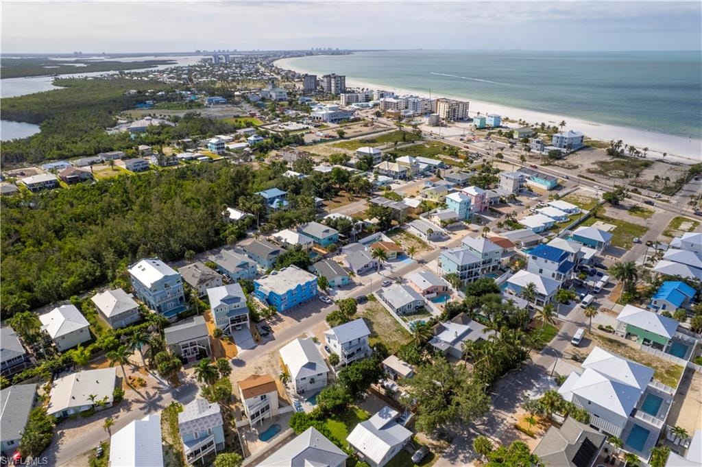Aerial perspective showcasing a coastal community with numerous residences, proximity to a white sand beach, and expansive water bodies