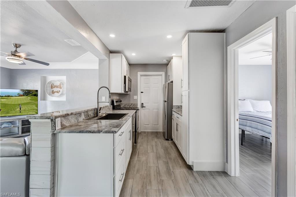 Kitchen featuring white cabinetry, granite countertops, stainless steel appliances, and wood-finish flooring