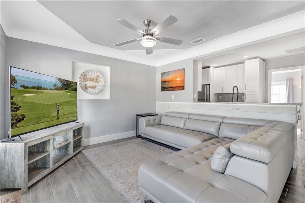 Open-concept living space featuring wood-finish tile flooring, a recessed ceiling with a ceiling fan, and a kitchen pass-through with a built-in counter