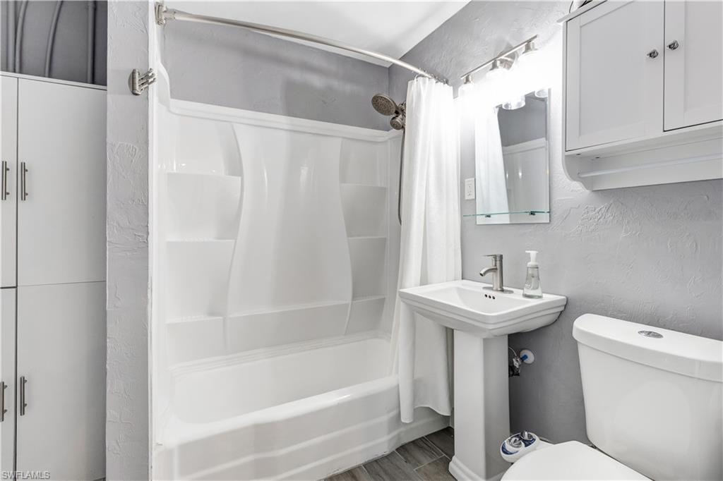 Bathroom featuring a white shower-tub combination, pedestal sink with chrome faucet, toilet, and white built-in cabinetry