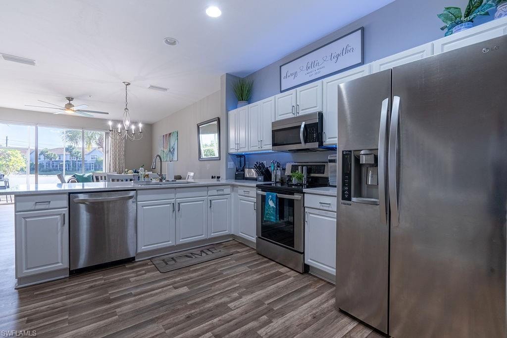 Kitchen featuring appliances with stainless steel finishes, white cabinets, hanging light fixtures, a chandelier, and light countertops