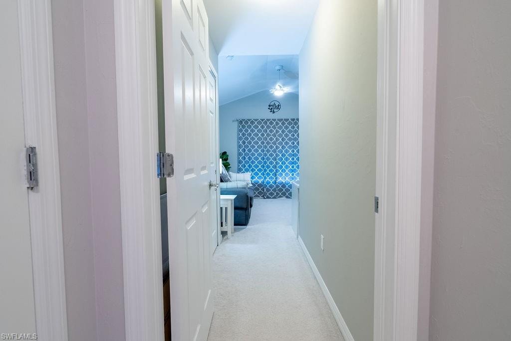 Corridor featuring vaulted ceiling and light colored carpet